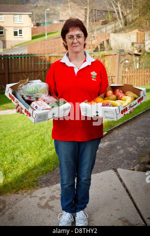 Eine Frau hält zwei Gemüse Boxen vor ihrem Haus auf einer Südwales-Siedlung, die sie von einem Veg Co-op erhält Stockfoto