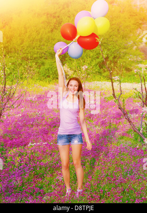 Glückliche junge Frau hält in Händen viele bunte Luftballons, Feld, Sommer Zeit Saison Spaß auf lila Blumen Stockfoto