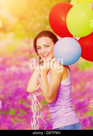 Süße fröhliche Frau, die Spaß mit Haufen von bunten Luftballons im Frühlingsgarten, Geburtstagsfeier, Glück-Konzept Stockfoto