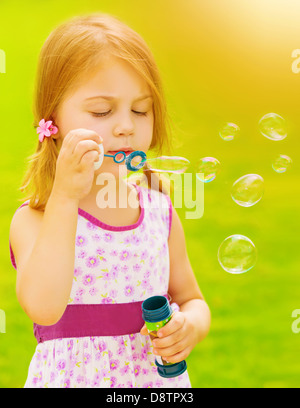 Closeup Portrait von niedlichen Babymädchen bläst Seifenblasen im freien Spiel auf Frühlingsgarten, sonnigen Tag, glückliche Kindheit Stockfoto