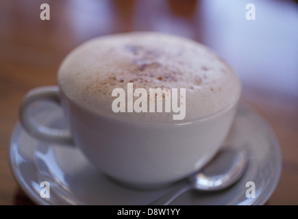 Cappuccino (Milchschaum Kaffee) in eine weiße Tasse mit Untertasse und Teelöffel auf braunen Tisch mit geringen Schärfentiefe Stockfoto