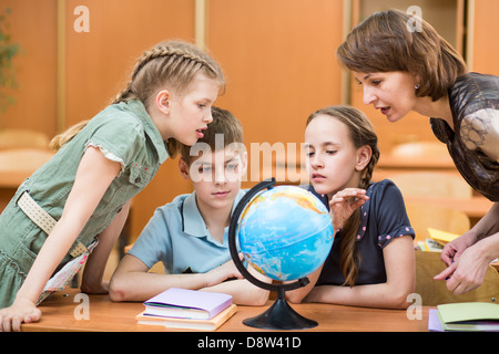 Schülerinnen und Schüler studieren einen Globus zusammen mit Lehrer Stockfoto