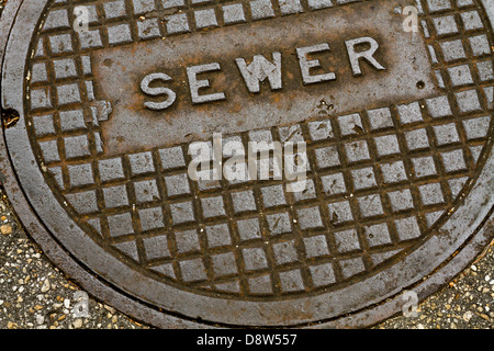 Eine alte Grunge Stahl Metall Kanalisation Kanaldeckel in einer Seitenstraße der Asphalt gepflastert. Stockfoto