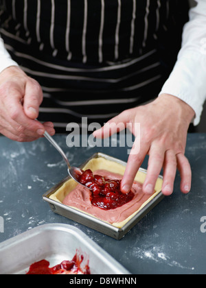 Der Konditor-Creme Inverkehrbringen Erdbeeren-Marmelade in der Mitte des Kuchens Stockfoto