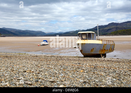 Fairboune Strand auf der Küste von Barmouth Bay, Gwynedd, Wales, UK mit verrosteten alten Boot und Barmouth Mautbrücke in der Ferne Stockfoto