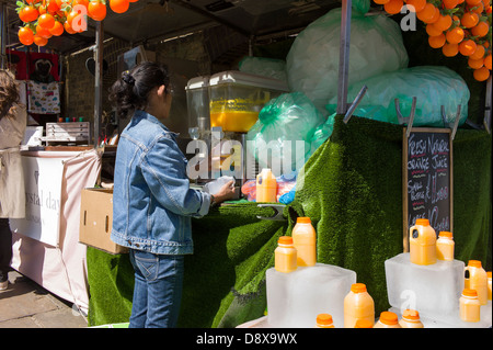 London UK, Camden Town, Camden Market, Frau machen, quetschen frisch gepressten Orangensaft am Marktstand, Stockfoto