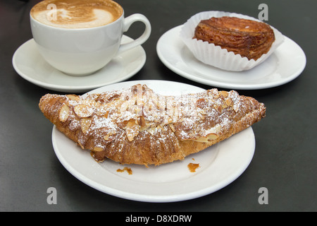 Mandel-Croissant Blätterteig auf weißen Teller mit Tasse Latte Stockfoto