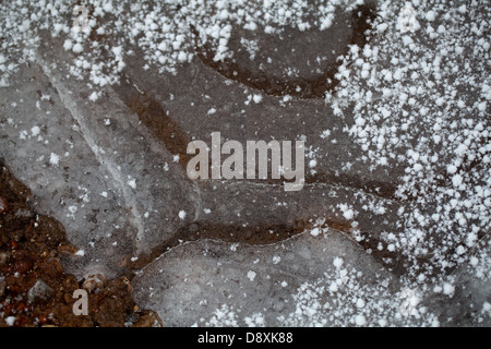 Gefrorene Pfütze auf einem ländlichen Weg. Zeigt gefallenen Hagelkörner am Boden und auf dem Eis. Stockfoto