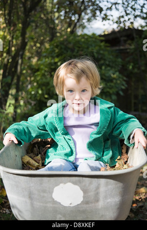Drei-jähriges Mädchen sitzt in einer Badewanne voller Blätter Stockfoto