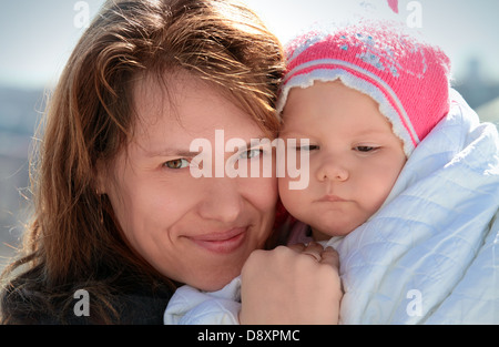 Junge europäische Frau hält ihr verschlafenes kleines Mädchen in Decke Stockfoto