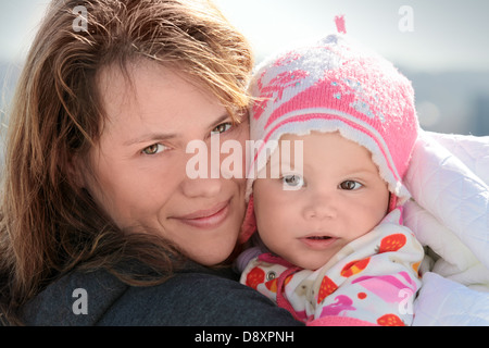 Junge Frau hält ihr verschlafenes kleines Mädchen in Decke. Outdoor Closeup portrait Stockfoto