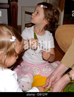 Großmutter und kleine Mädchen (4 und 2 Jahre alt) schälen Erbsen zu Hause Stockfoto