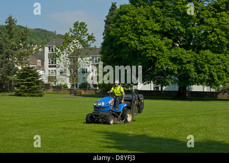 Des Rates Mitarbeiter mit Reiten-auf Rasenmäher, Mähen im kleinen Park, Kendal, Cumbria, England UK Stockfoto