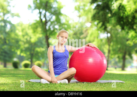 Junge Frau im sitzen auf einem grünen Rasen mit Pilates Ball im Park Sportbekleidung Stockfoto