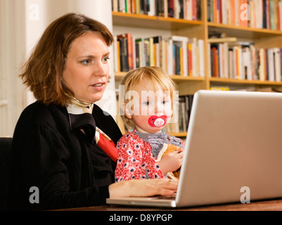 Frau mit Tochter am Schoß Arbeit an laptop Stockfoto