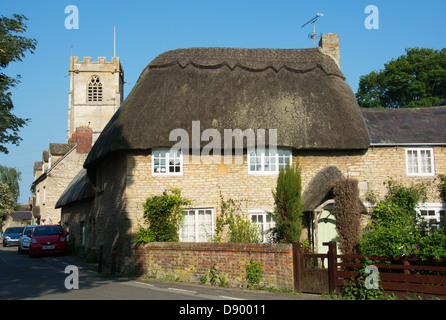 OXFORDSHIRE, VEREINIGTES KÖNIGREICH. Eine strohgedeckte Hütte mit einer Kirche hinter in dem Dorf Eynsham in der Nähe von Witney. 2013. Stockfoto