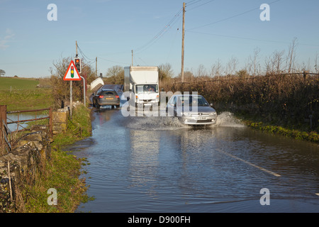 Der Verkehr bahnt sich seinen Weg durch eine überflutete Straße nach Winterregen, in der Nähe des Flusses Parrett, Martock, in den Somerset Levels, Somerset, Großbritannien. Stockfoto
