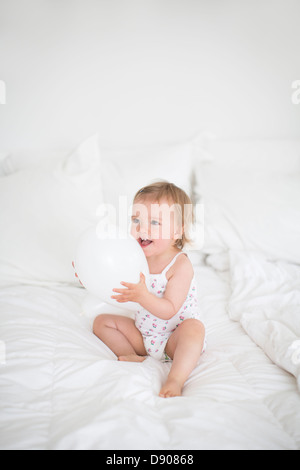 Kleines Mädchen sitzt auf dem Bett und hält Ballon Stockfoto