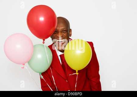 Ein Mann mittleren Alters trägt einen roten Anzug und hält Luftballons. Stockfoto