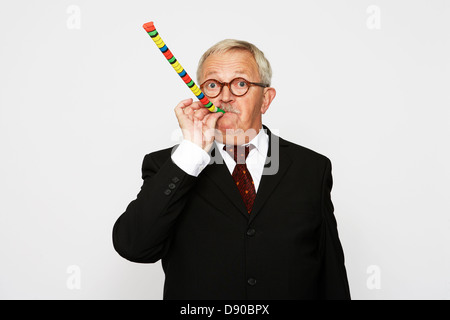 Ein älterer Mann in einem Anzug in einer Partei Horn Gebläse bläst. Stockfoto