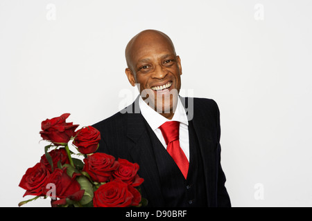 Ein Mann trägt einen Anzug und hält eine Buncht rote Rosen Stockfoto