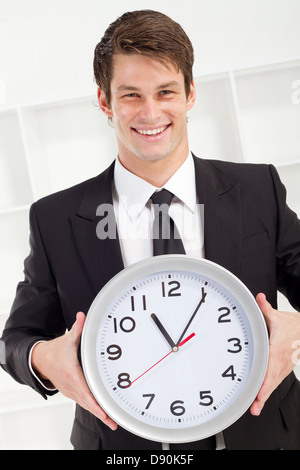 junger Geschäftsmann hält eine Uhr im Büro Stockfoto