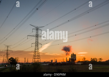 Sonnenuntergangsszene mit Hydro Towers und Stromleitungen mit Industriegelände im Hintergrund. Stockfoto