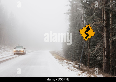 Ein LKW und ein Zeichen der Kurve bei Nebel und Schnee auf einer Bergstraße. Stockfoto