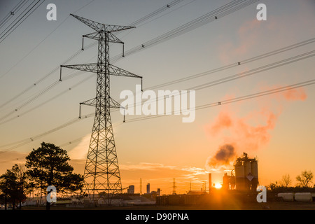 Sonnenuntergangsszene mit Hydro Towers und Stromleitungen mit Industriegelände im Hintergrund. Stockfoto