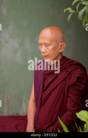 Erkennbar durch seine dunklen roten Roben burmesischen Mönch sitzt in der Kontemplation in einer Nische Seite der Shwedagon Pagode komplexe Stockfoto