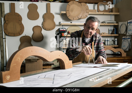 Gitarrenbauer arbeitet an Plänen für eine akustische Gitarre in Werkstatt Stockfoto