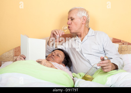 Lustige älteres paar entspannende im Bett mit Alkohol und Buch Stockfoto