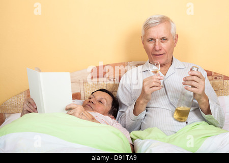 Älteres paar ruhen im Bett mit Alkohol und Buch Stockfoto