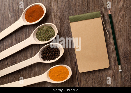 Notizbuch und Stift für Rezepte und Gewürze im Löffel auf Holztisch Stockfoto
