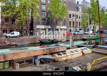 Boote und Reihenhäuser auf Geldersekade Kanal in Amsterdam, Niederlande, Nord-Holland Provinz. Stockfoto