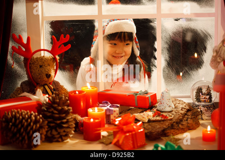 Mädchen betrachten Weihnachtsgeschenk durch Fenster Stockfoto