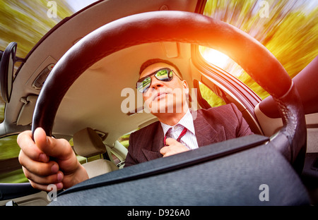 Mann in einem Anzug und Sonnenbrille auf einer Straße im Auto fahren. Stockfoto