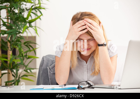 Reife Frau mit Kopfschmerzen am Tisch im Büro Stockfoto