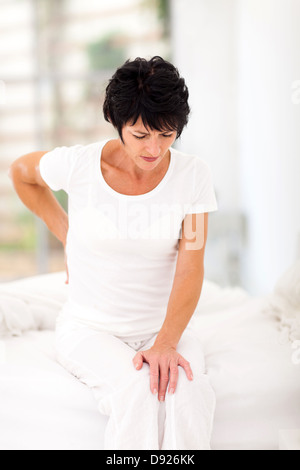 mittlere gealterte Frau sitzt auf Bett mit Rückenschmerzen Stockfoto