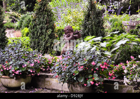 kleine Keramik Statue eines Fauns beim Flötenspiel zwischen bunten Blumen Stockfoto