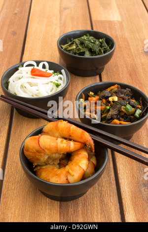 Asiatische vegetarische Nahrung zusammen mit vier schwarzen Schalen mit Garnelen, Reisnudeln, Kohl (Grünkohl), gebratenem Gemüse. Stockfoto