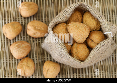 Ganze Walnüsse in Jute-Tasche auf Wicker Hintergrund, Nahaufnahme Stockfoto