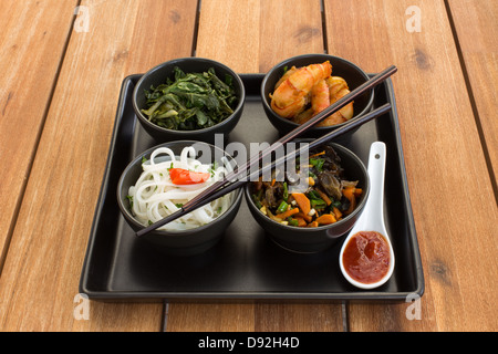 Asiatische Schale auf einer quadratischen Platte in schwarz Schalen mit Garnelen, Reisnudeln, Kohl (Grünkohl) und gebratenem Gemüse. Stockfoto