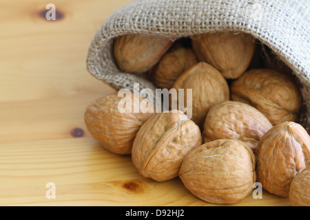 Ganze Walnüsse in Jute-Tasche auf der Holzoberfläche, Nahaufnahme Stockfoto