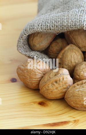 Ganze Walnüsse in Jute-Tasche auf der Holzoberfläche, Nahaufnahme Stockfoto