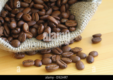 Kaffeebohnen in Jute-Tasche auf der Holzoberfläche, Nahaufnahme Stockfoto