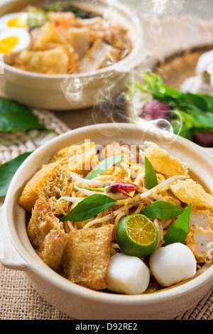 Scharf und würzig malaysische Curry Nudeln oder Laksa mir mit heißem Wasserdampf im Tontopf, Dekoration Einrichtung dienen mit Stäbchen. Malaysia-Küche. Stockfoto