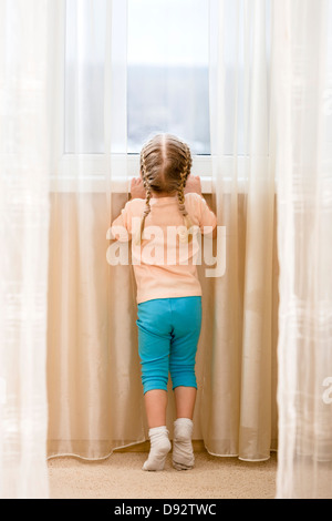 Kleines Mädchen auf ihren Zehenspitzen aus Fenster sehen wollen Stockfoto