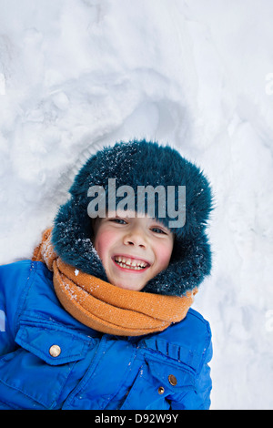 Ein fröhlicher Junge tragen warme Kleidung im Freien im Schnee liegen Stockfoto