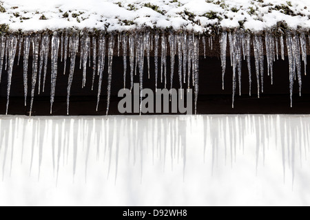 Schnee und eine Reihe von Eiszapfen hängen von der Traufe eines Gebäudes Stockfoto